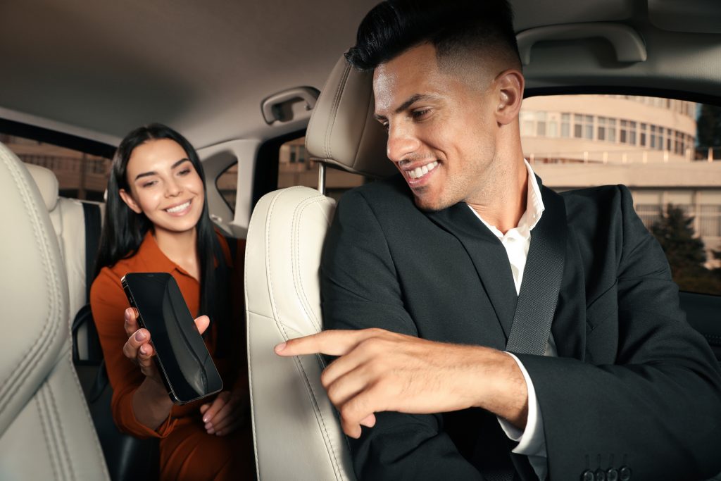 Young woman showing smartphone to taxi driver in modern car